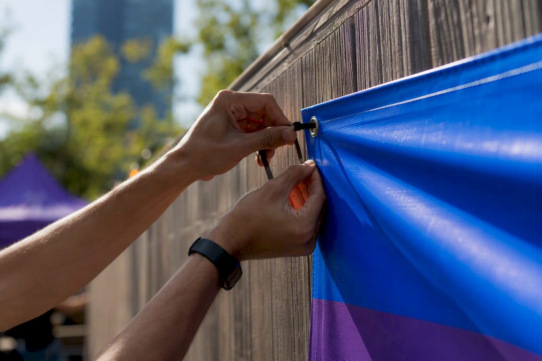 Hands fastening vinyl banner on outdoor fence