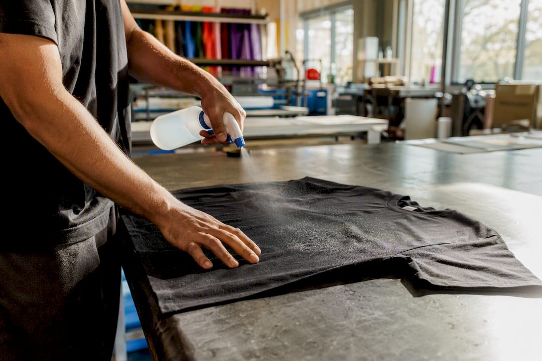 Hands spraying pretreatment on dark fabric