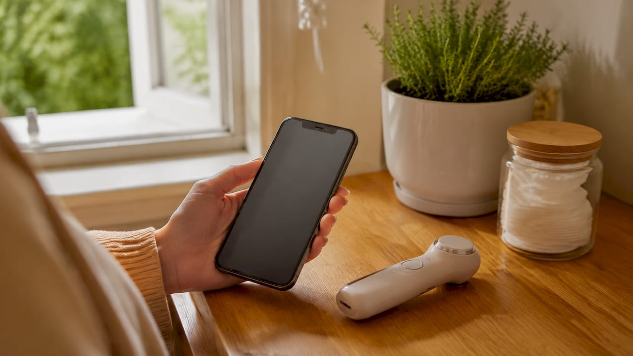 Hands holding smartphone near beauty device on countertop