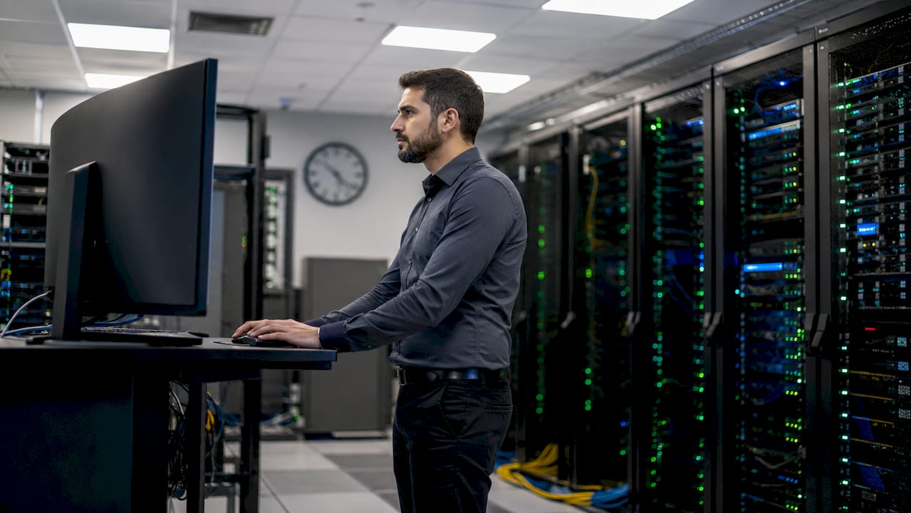Tecnico al lavoro sulla tastiera, circondato dai server nel data center.