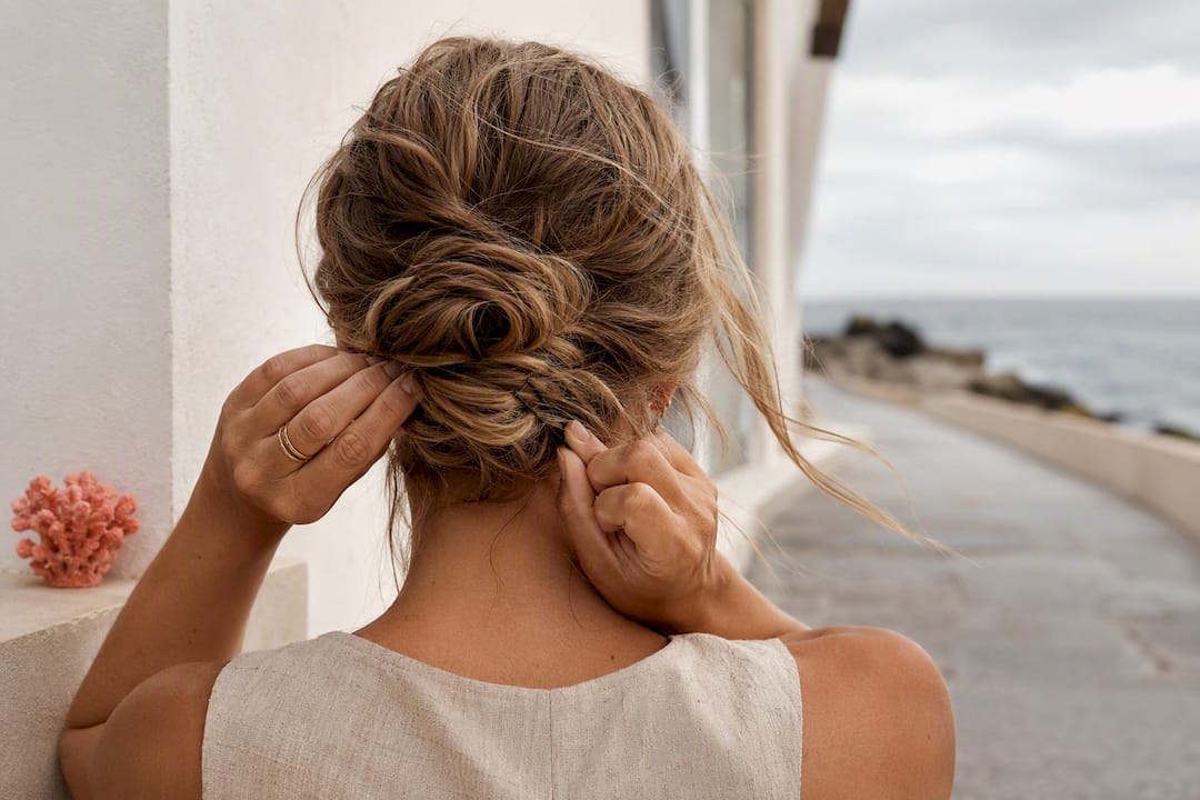 Hands securing a low bun in sea breeze