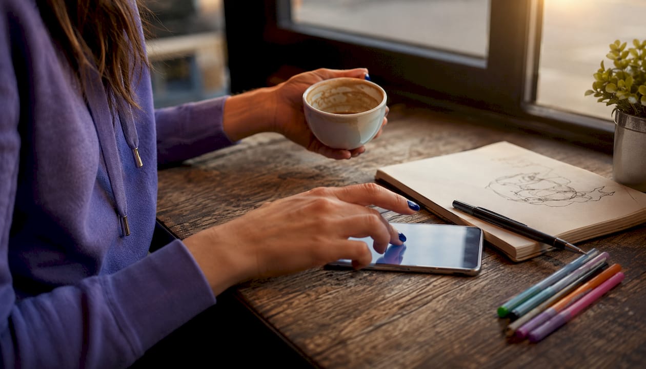 Hands hesitant over smartphone in café