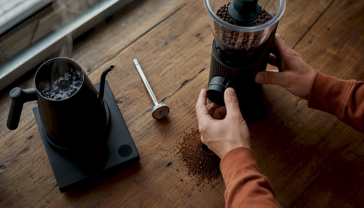 Hands adjusting burr grinder in kitchen setting