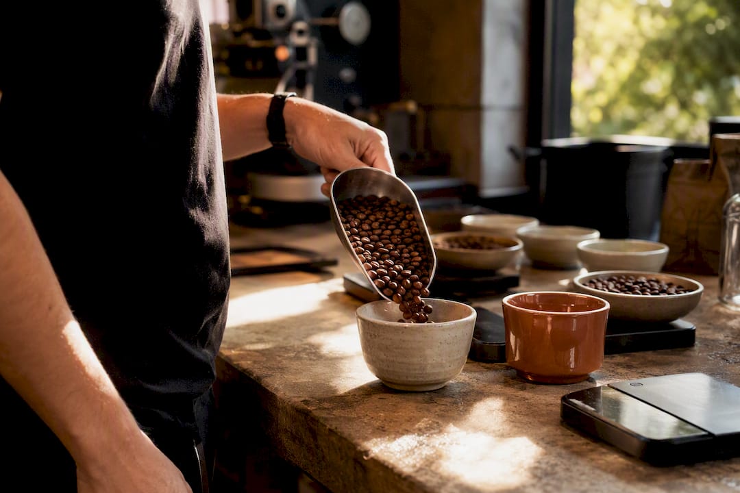 Roaster pouring single-origin coffee beans into cupping bowl