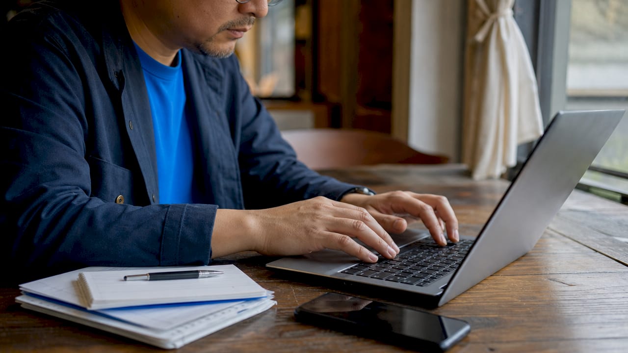 Hands typing on laptop with checklists nearby