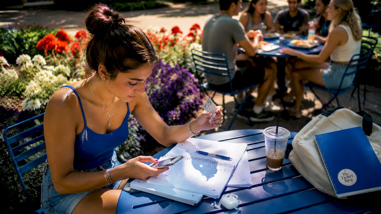 Student buying sports tickets on phone in cafe