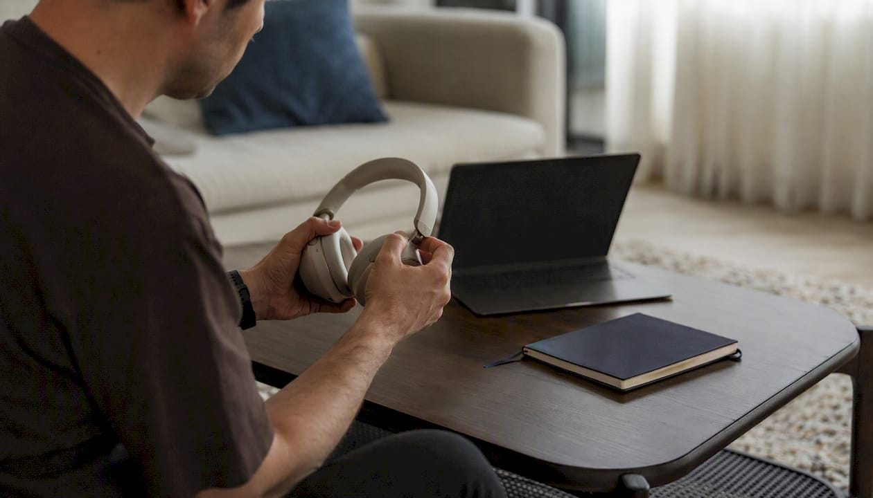 Hands adjusting headphones beside laptop and notepad