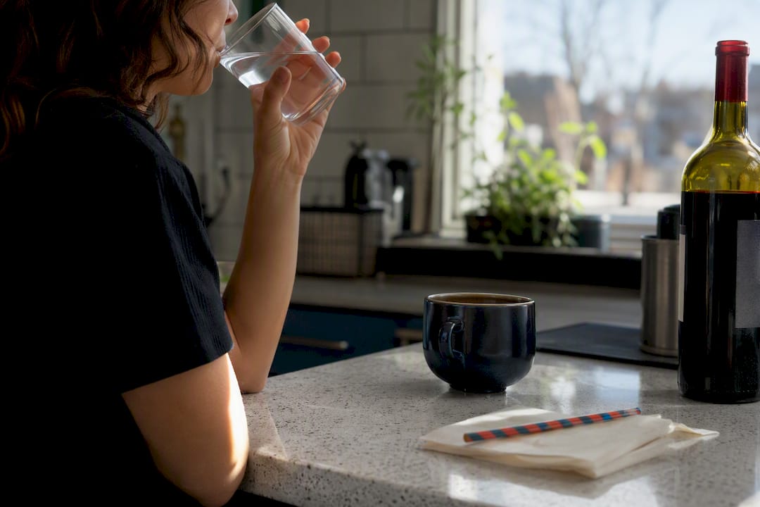 Hand holding glass of water near coffee and wine