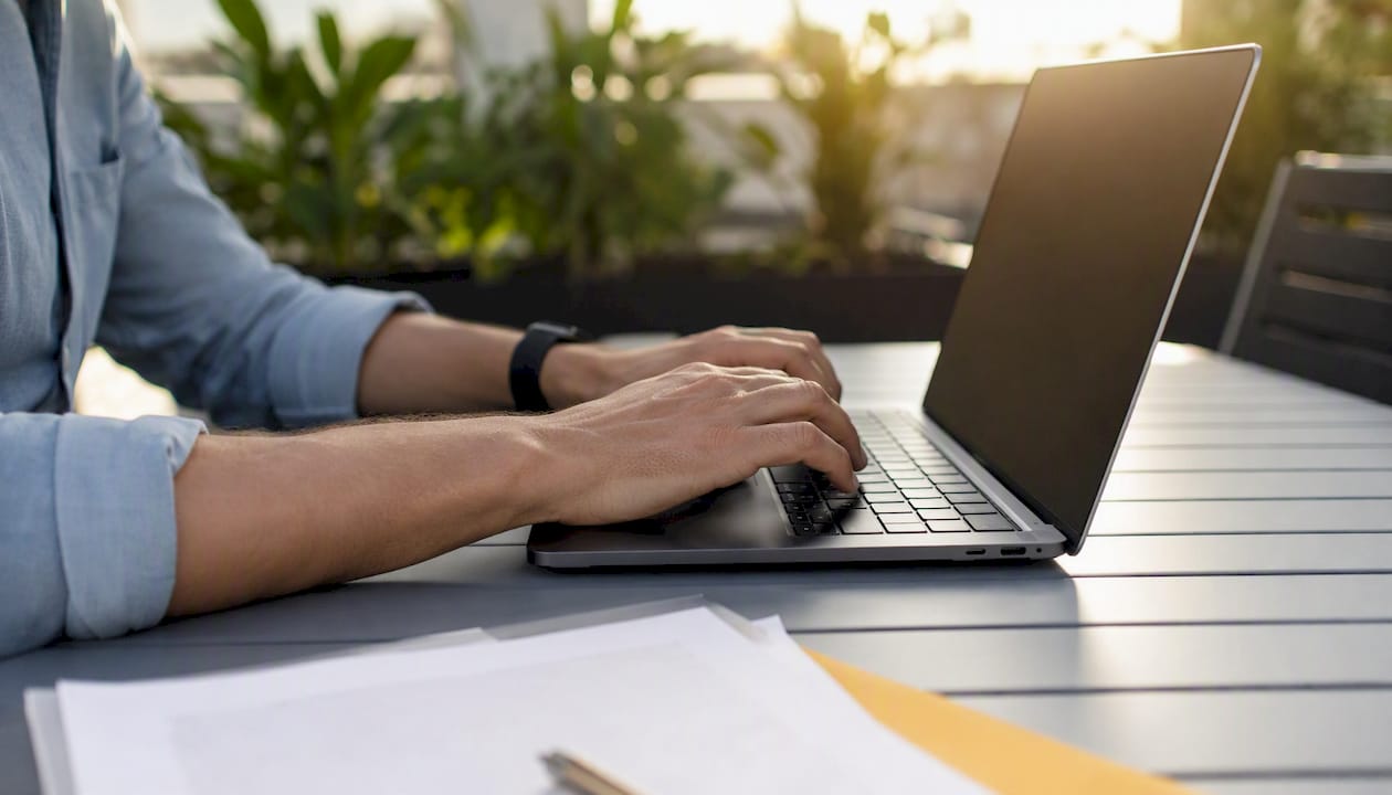 Hands typing on laptop with patent materials nearby