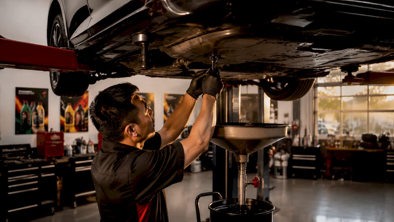 Mechanic changing car oil under vehicle