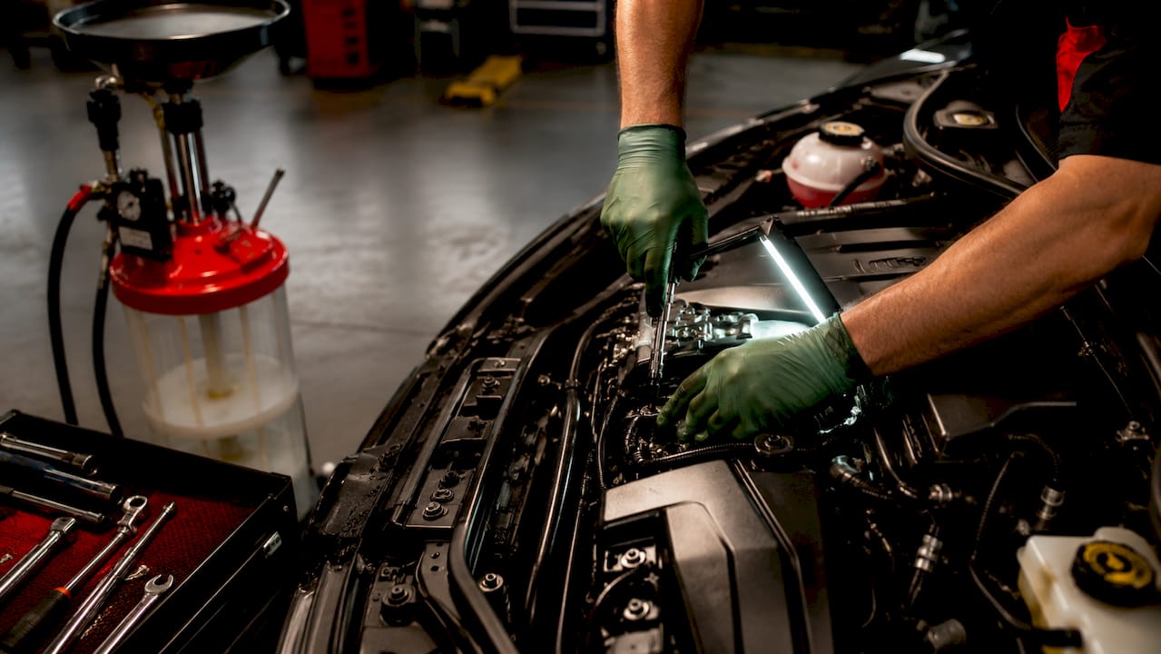 Mechanic performing oil change under car hood
