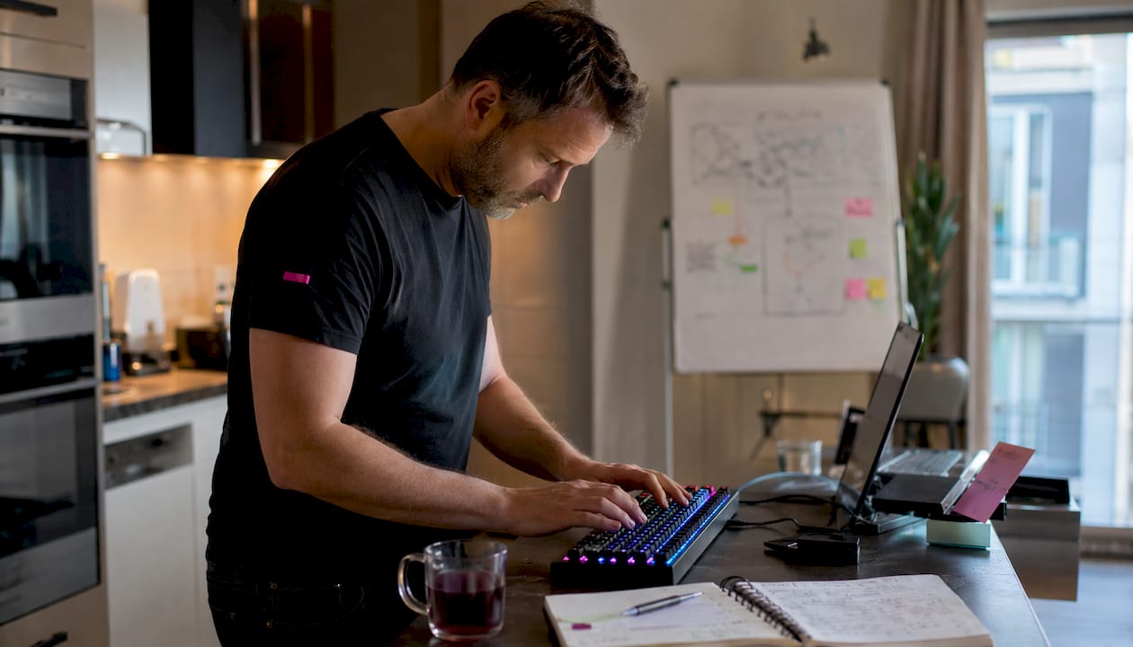 Des mains qui s’activent sur un clavier, entourées de post-it collés au mur.