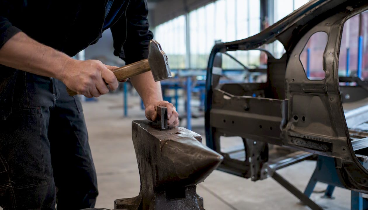 Des mains expertes travaillent le métal, façonnant avec précision une pièce de châssis automobile.