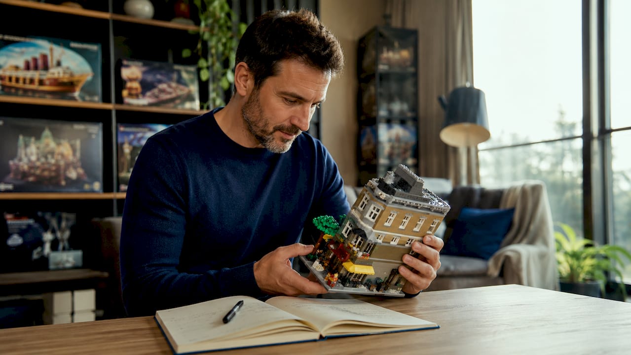 Un homme observe attentivement une boîte de LEGO dans son bureau, visiblement passionné par sa nouvelle trouvaille.