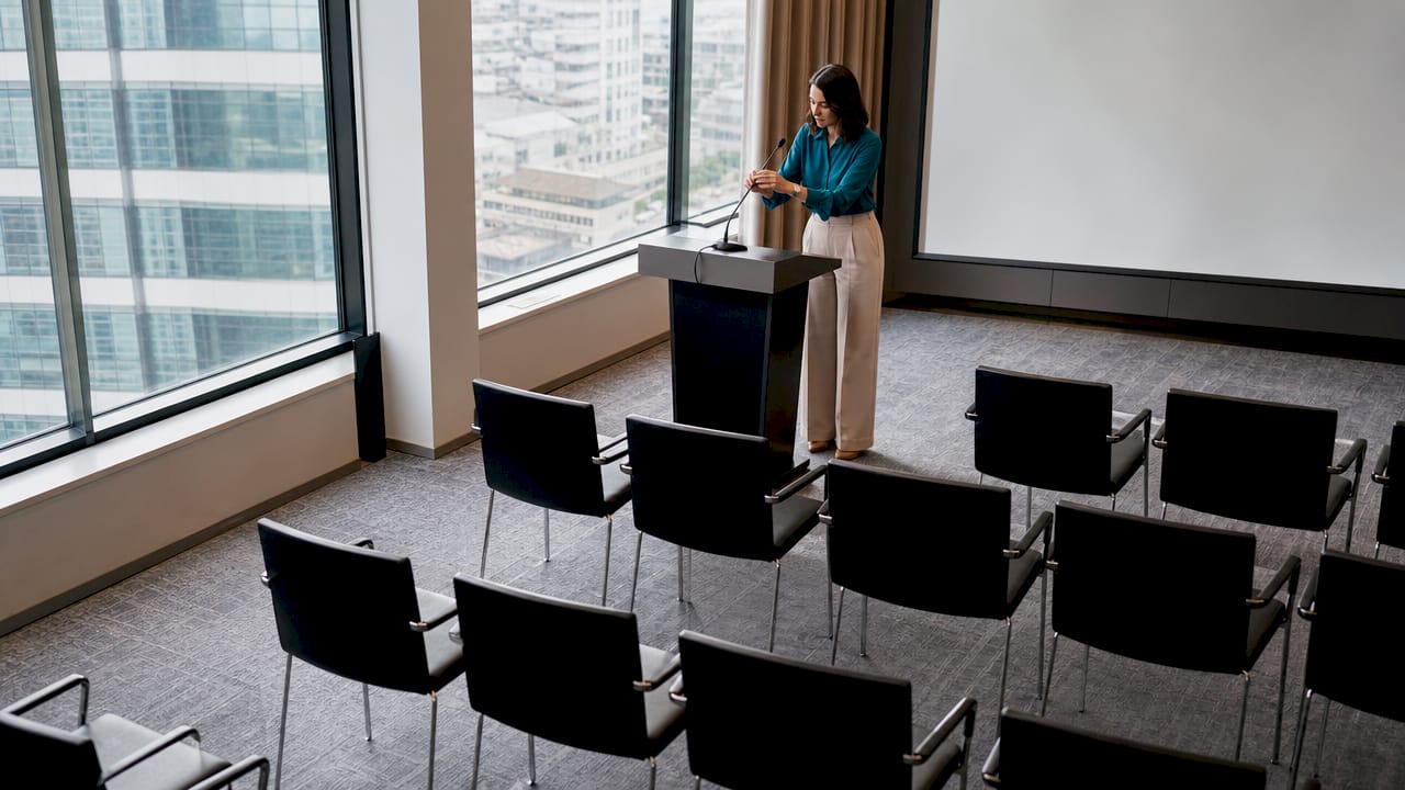 Panoramica della sala conferenze pronta per l’evento, mentre il relatore sistema il microfono prima di iniziare.