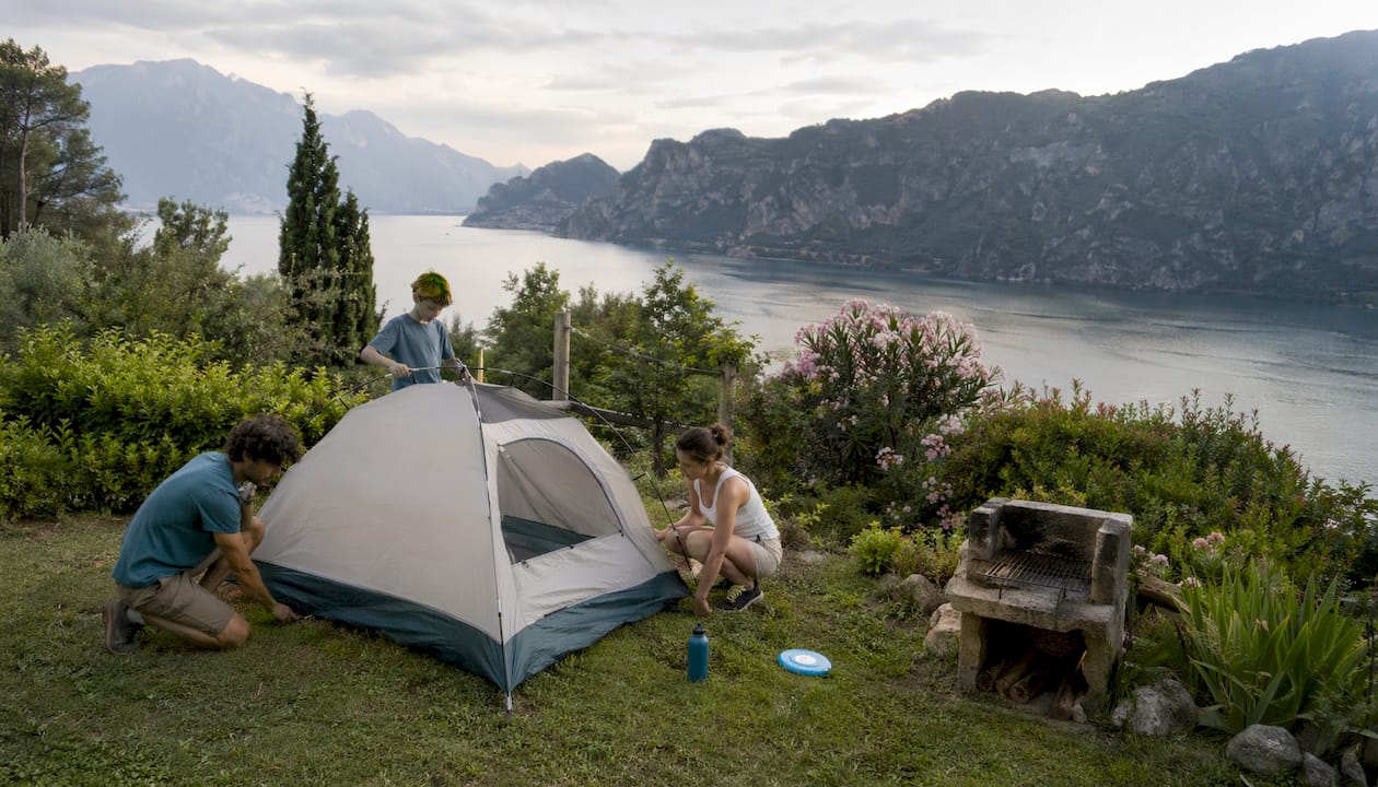 Un gruppo di amici monta la tenda per il campeggio sulle rive del Lago di Garda.