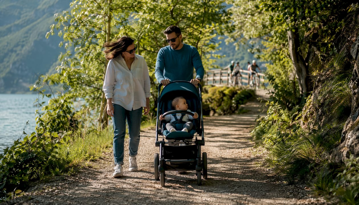 Una coppia di genitori passeggia lungo un viale ombreggiato spingendo il passeggino.