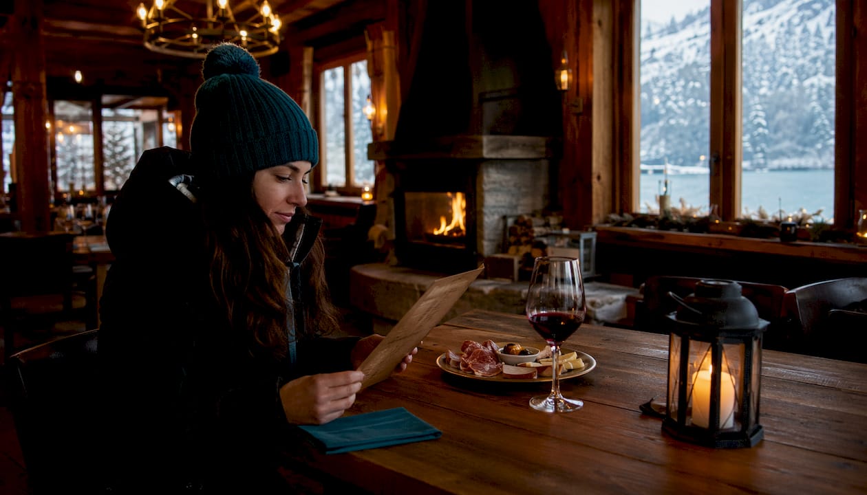 Una donna sfoglia il menù seduta al tavolo di un ristorante, mentre fuori l’inverno si fa sentire.