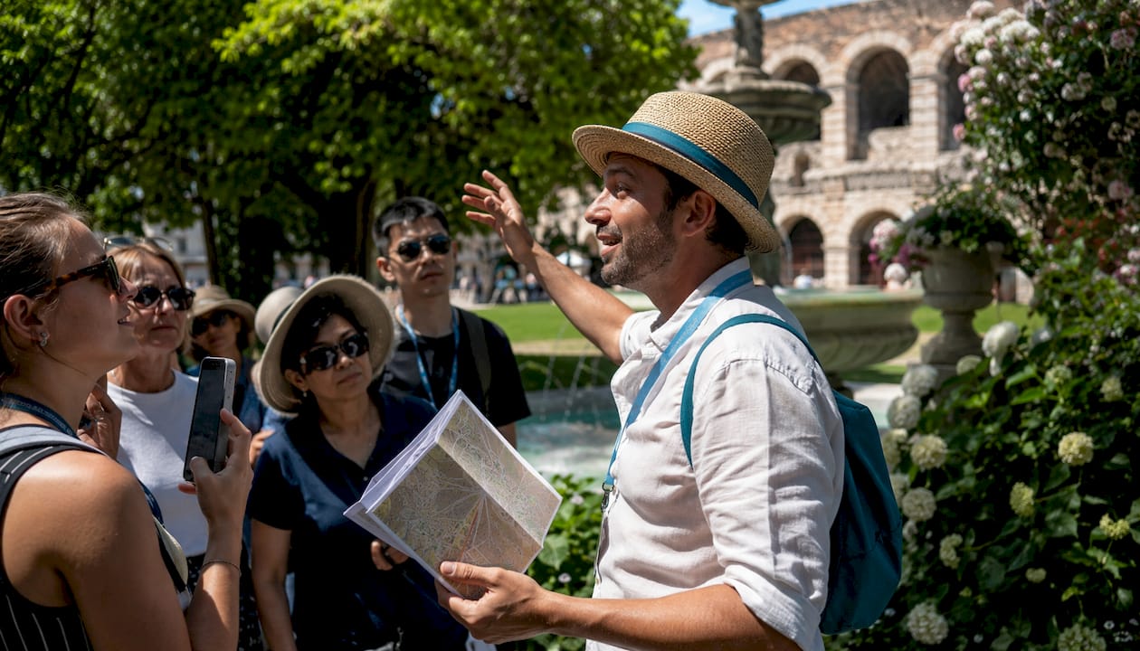 Una guida accompagna un gruppo di visitatori nei pressi dell’Arena, raccontando curiosità e storia del luogo.