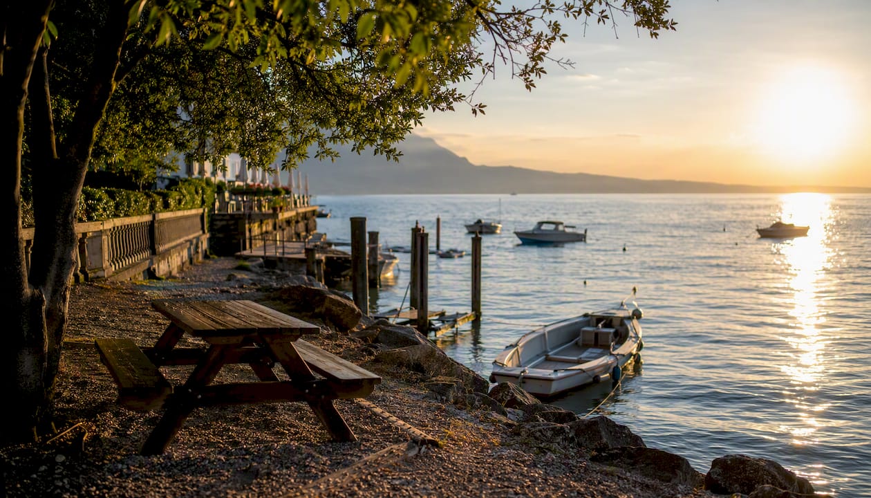 Splendida vista panoramica sul Lago di Garda, con barche che solcano le acque e il lungolago che invita a passeggiare.