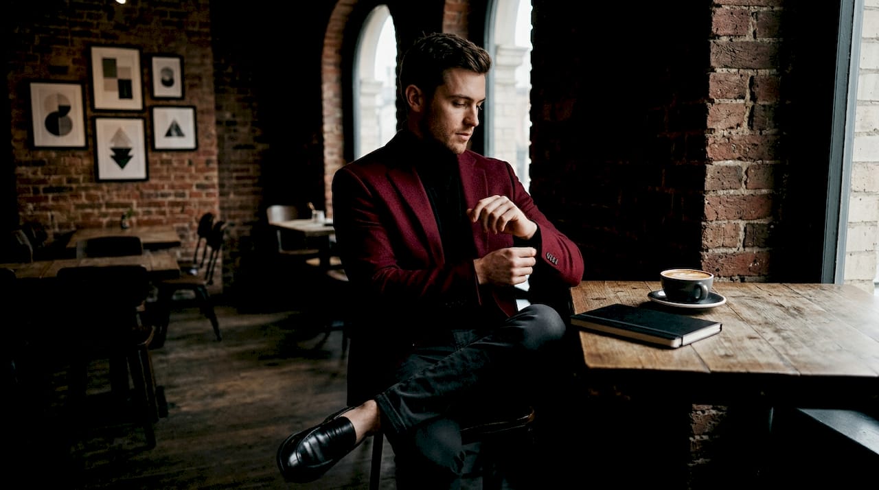 Man in burgundy blazer multitasking at cafe table