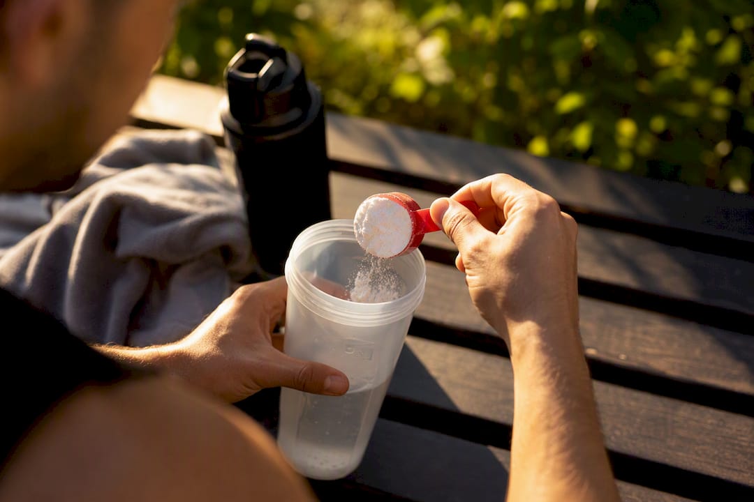 Hands measuring creatine powder into shaker bottle