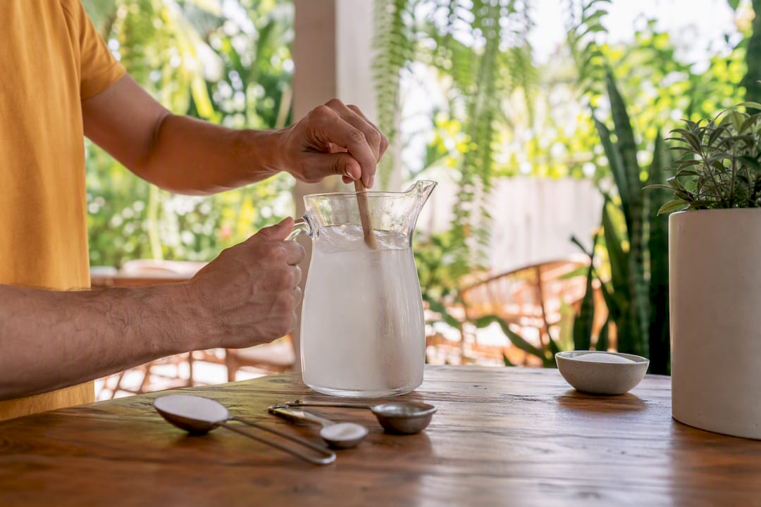 Hands mixing homemade electrolyte solution in jug