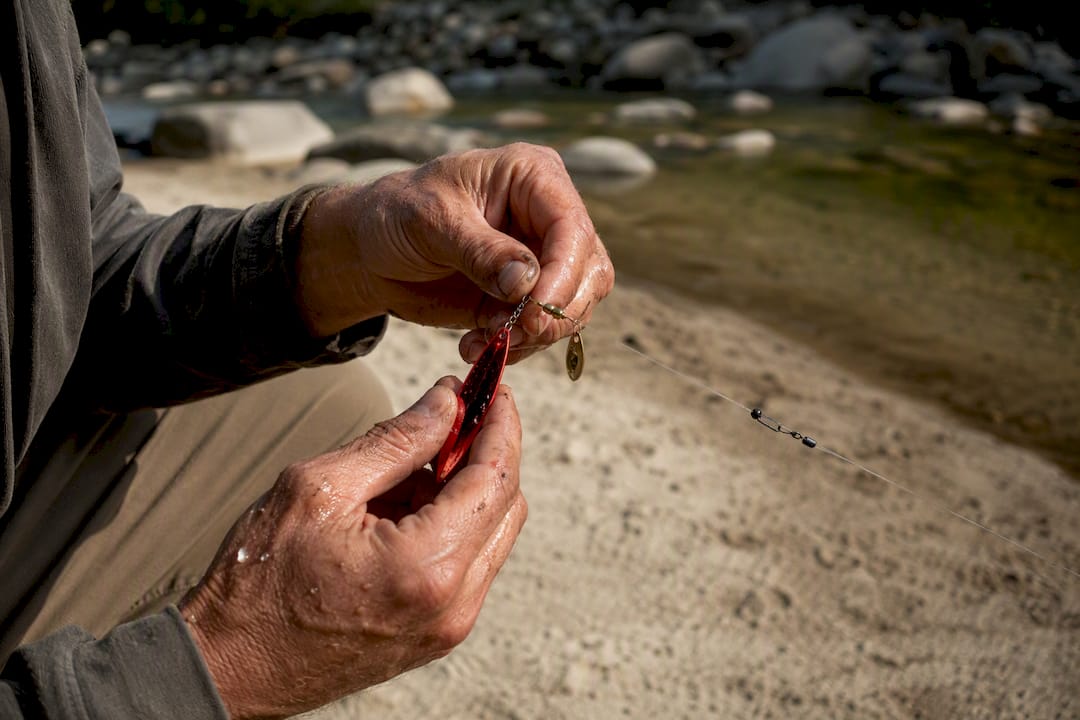 Angler hands adjusting spinner blade at riverbank
