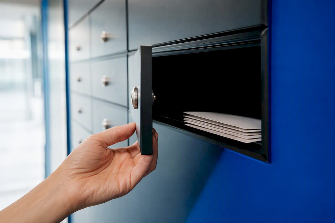 Eine Hand öffnet das Fach eines Geschäftsbriefkastens.