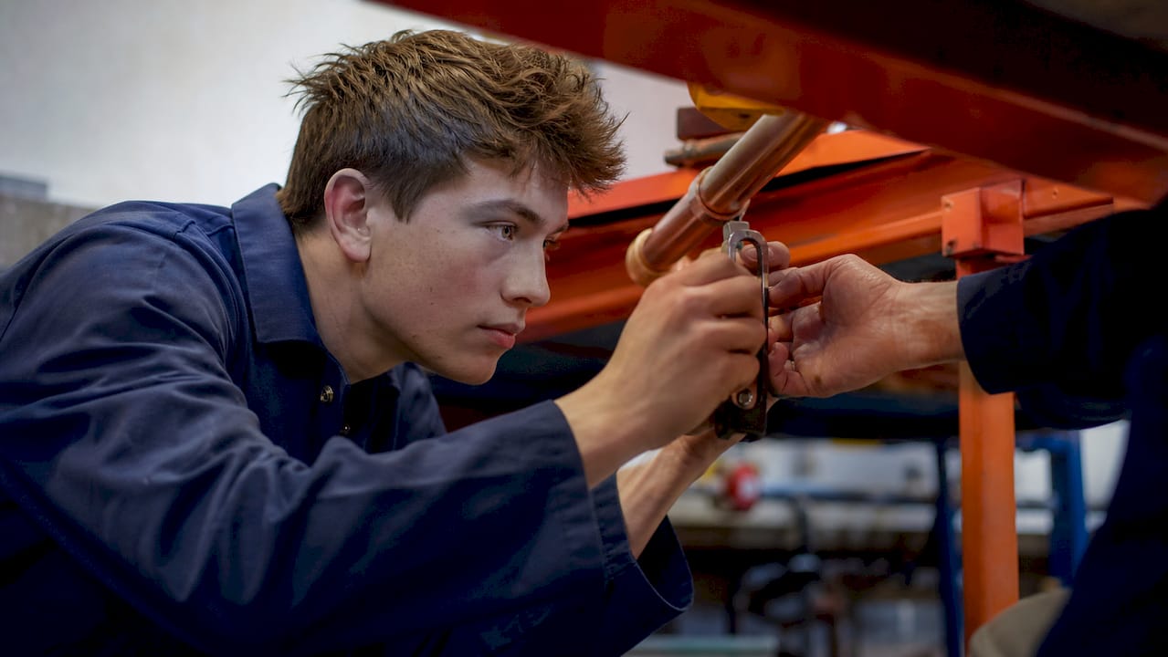 Apprentice tightening pipe clamp under mentor guidance