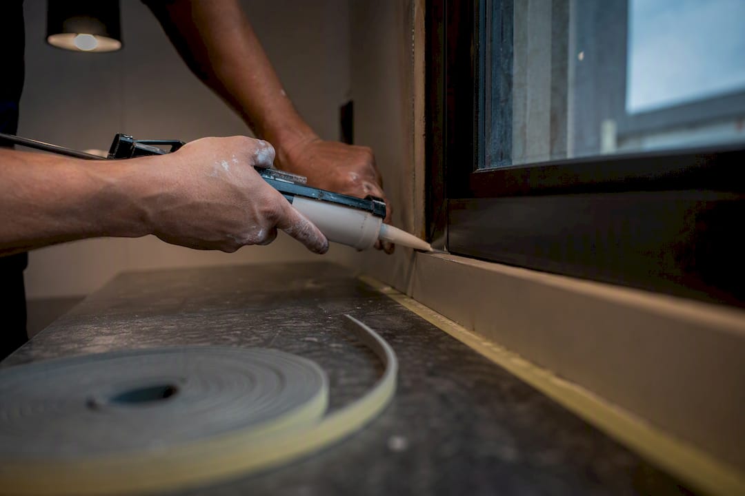 Hands applying acoustic caulk to window frame