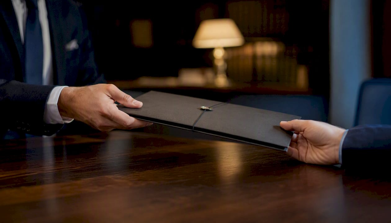 Hands exchanging sealed agreement folder