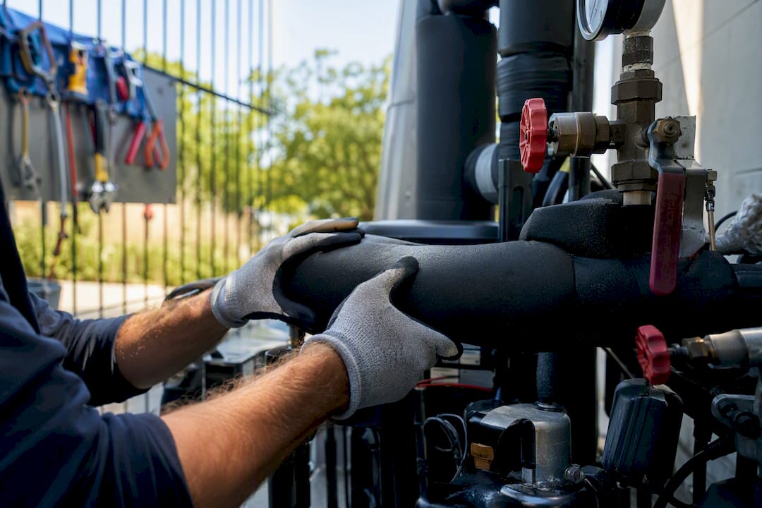 Hands inspecting HVAC pipes in school utility room