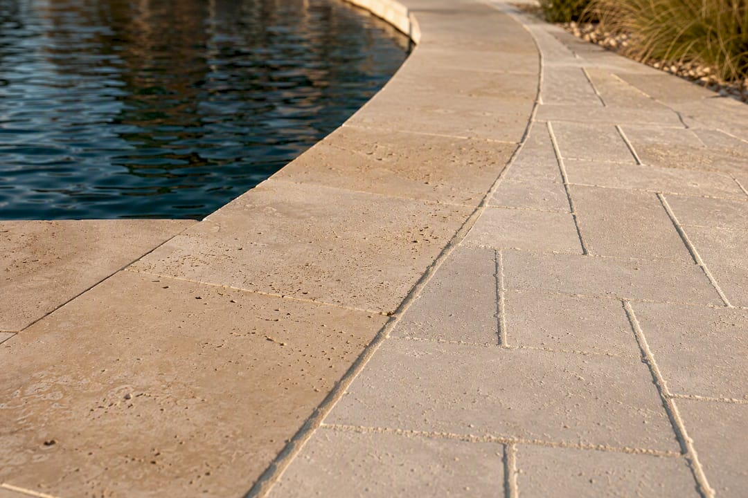 Travertine coping beside light paver decking