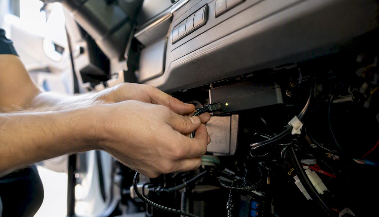 Hands connecting telematics unit inside vehicle dashboard