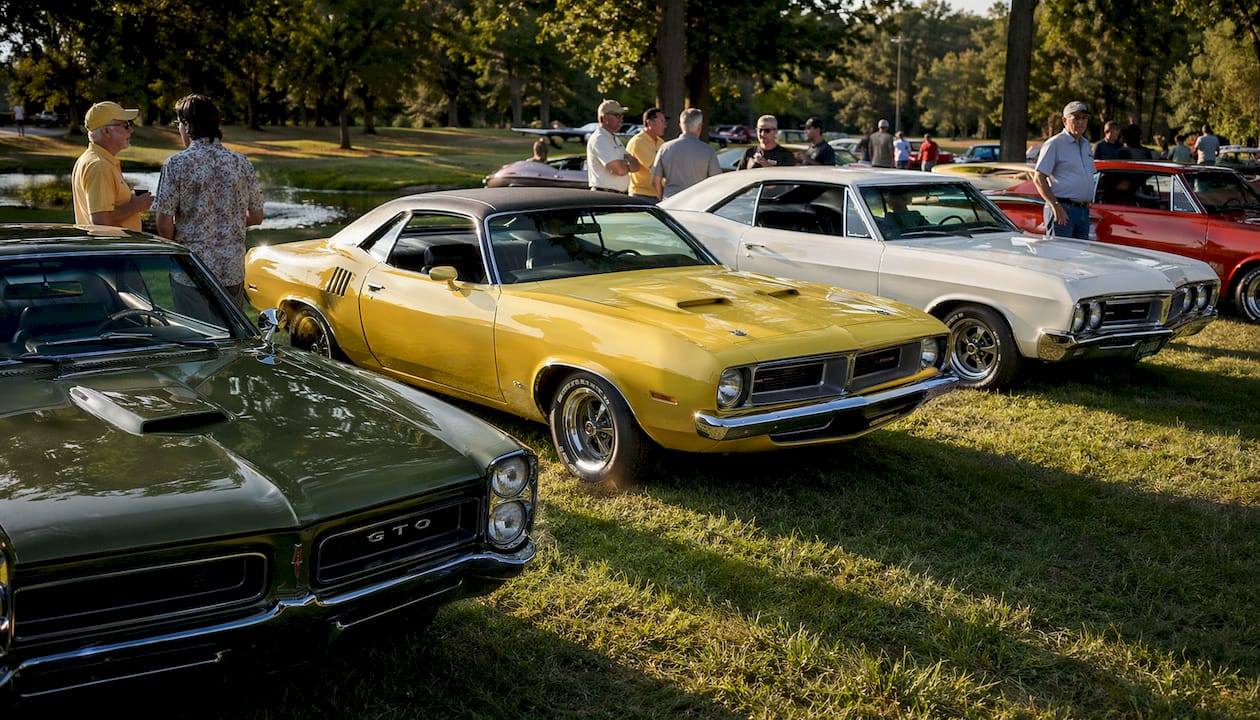 Outdoor lineup of classic muscle cars with enthusiasts
