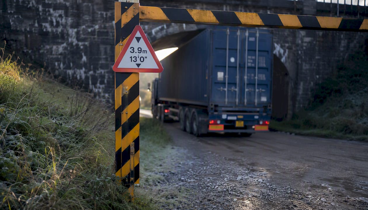Container truck near low railway arch bridge