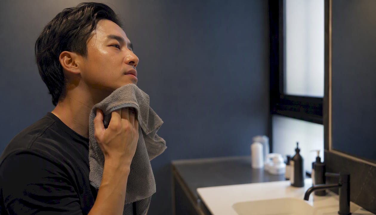 Man patting oily skin dry in bathroom mirror