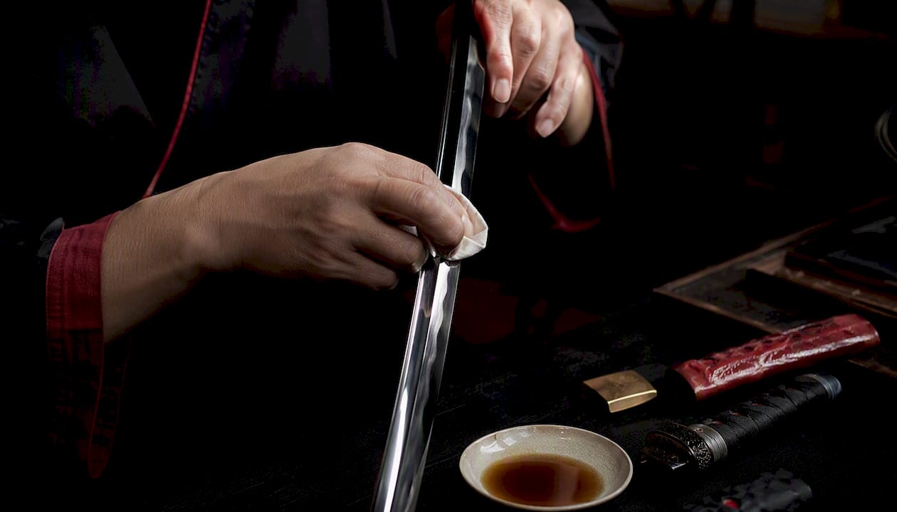 Hands oiling katana blade in workshop