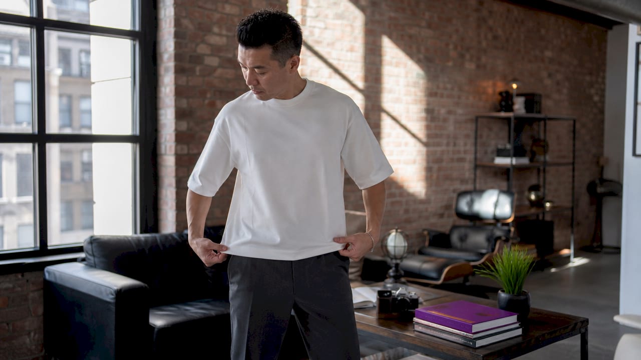 Man adjusting front tuck of graphic tee in living room