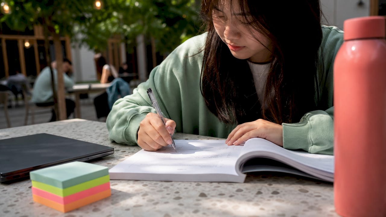 Hands writing notes on Bocconi admission prep booklet