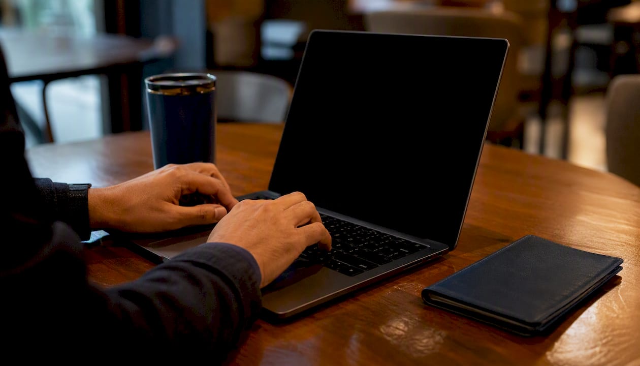 Hands near laptop with dark screen on desk