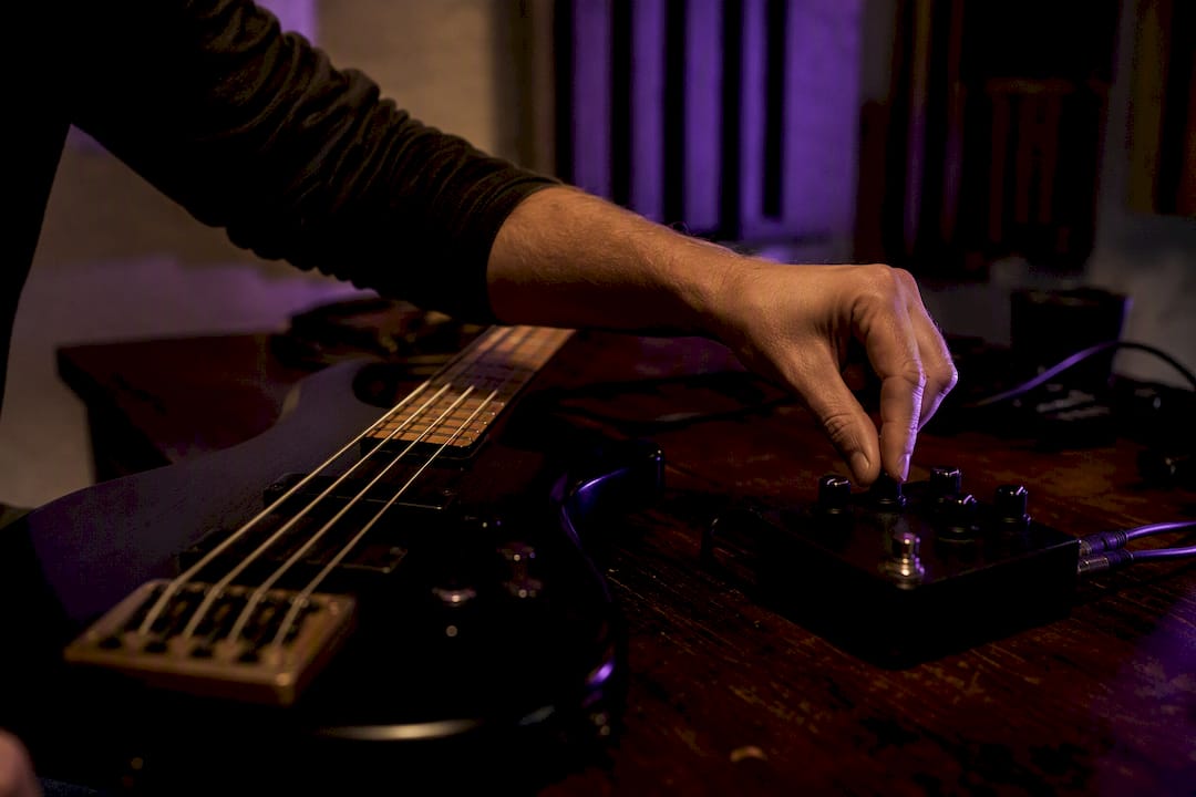 Hand adjusting distortion pedal knob on bass guitar studio table