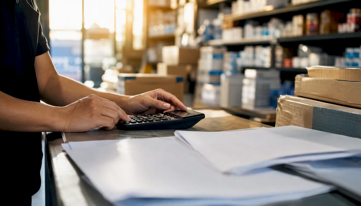 Hands calculating landed cost with documents
