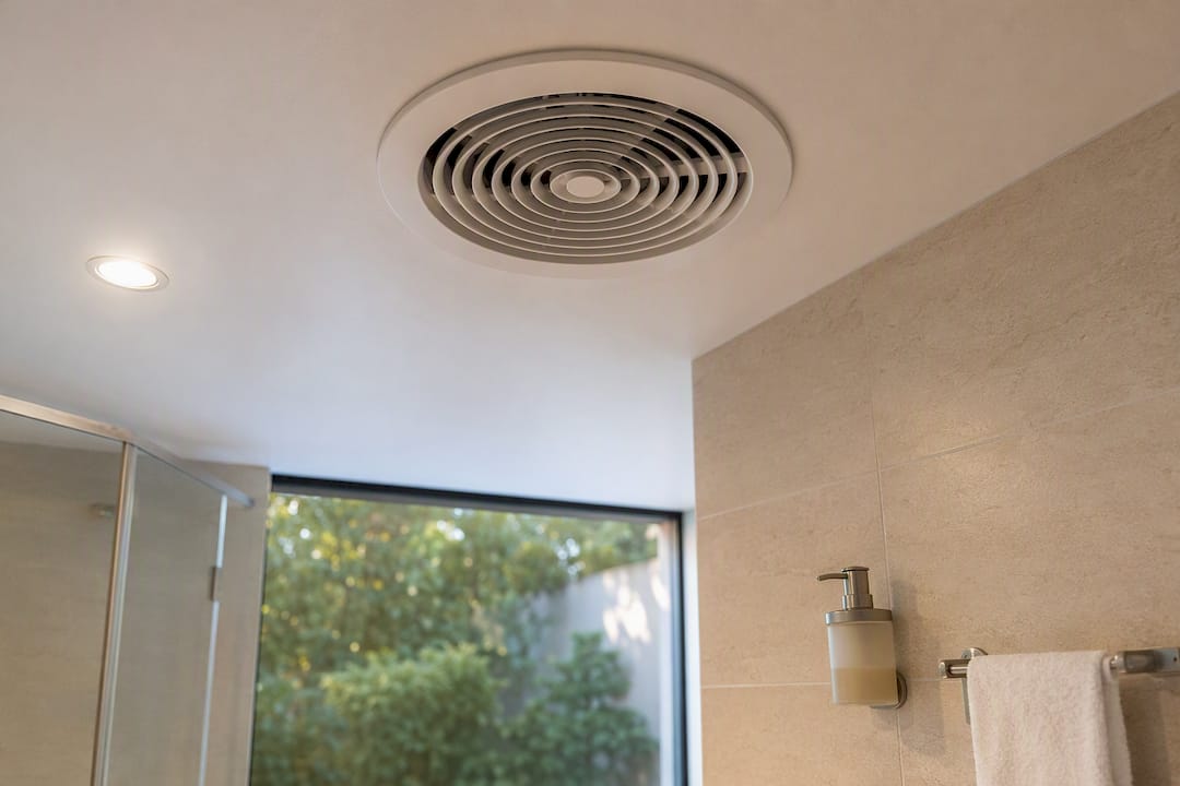Ventilador axial instalado en el baño, con salida de aire a través de un conducto corto.
