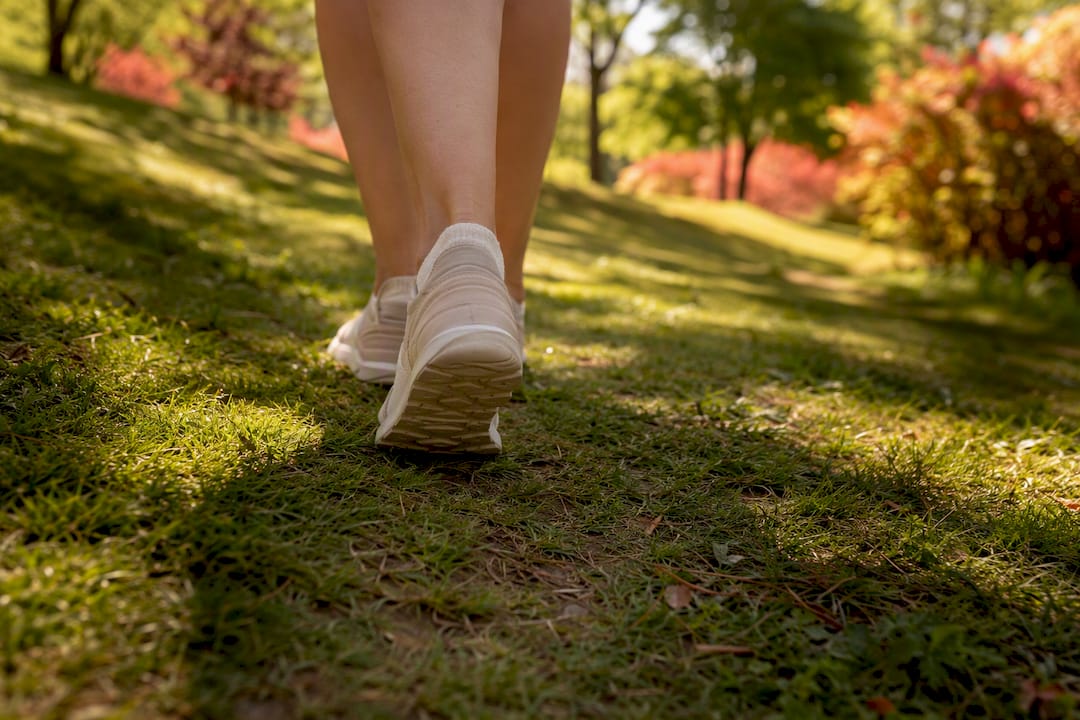 Feet walking on leaf-covered path outdoors