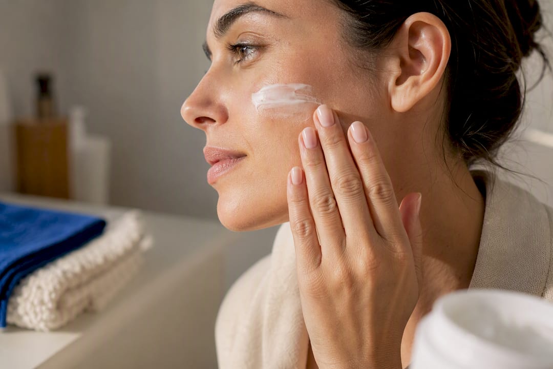 Mano aplicando crema facial en la mejilla
