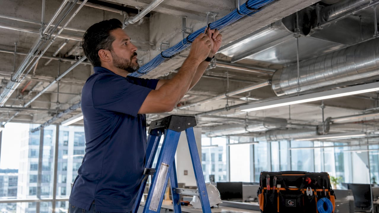 Technician managing cables on J-hooks in open ceiling office