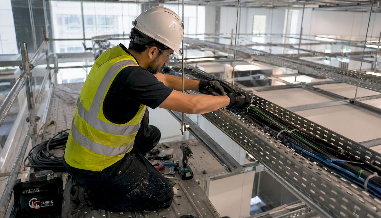 Technician installing cable tray in office ceiling