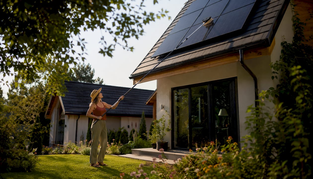 Woman cleaning solar panels from garden with pole brush